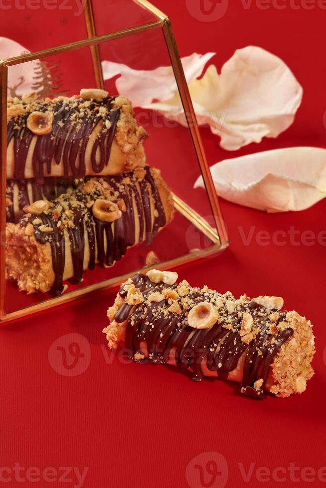 Delicious hazelnut and chocolate mini cakes reflecting in a golden glass box on red background with petals photo