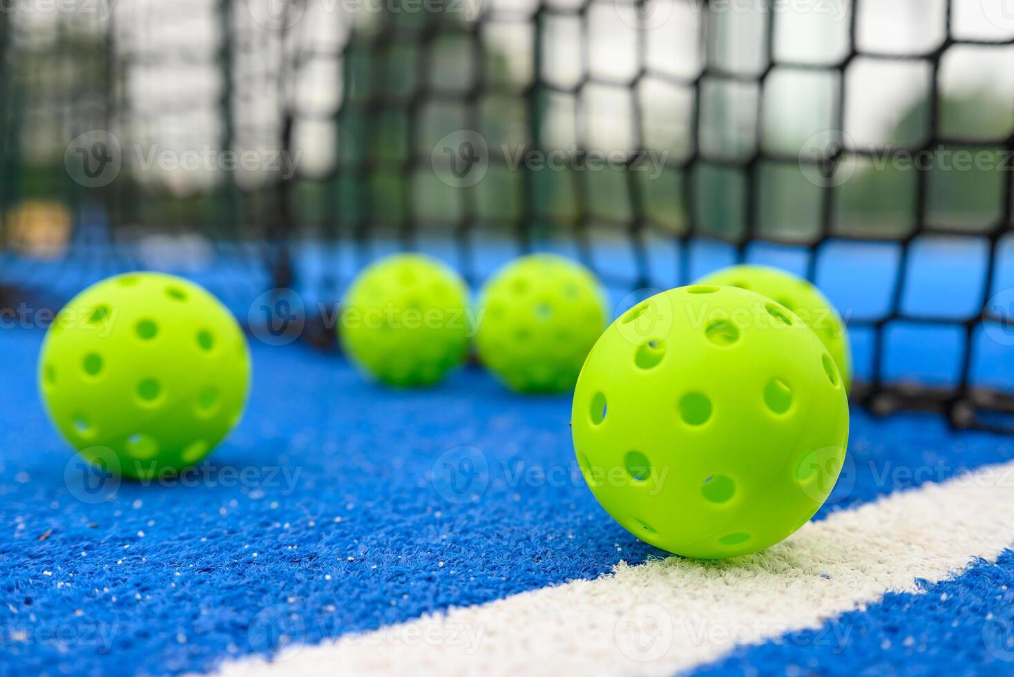 six pickleball balls near the net in a blue court, level surface view photo