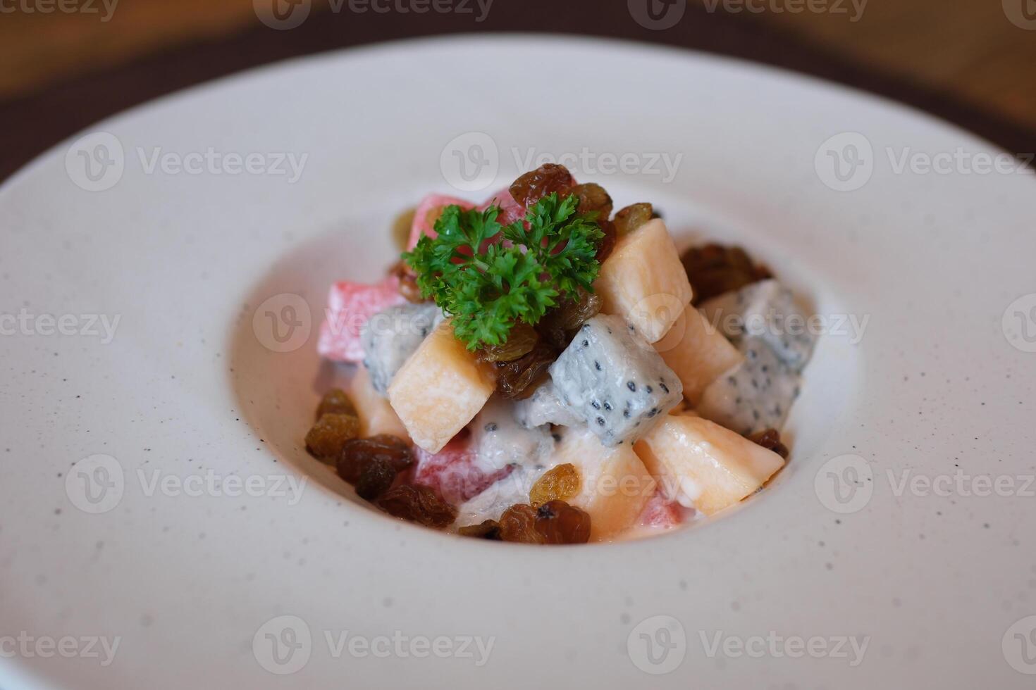 fruit salad with melon watermelon white precious fruit and raisins topped with yogurt on a white deep plate photo