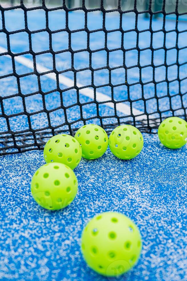 six green pickleball balls near the net in a blue court photo