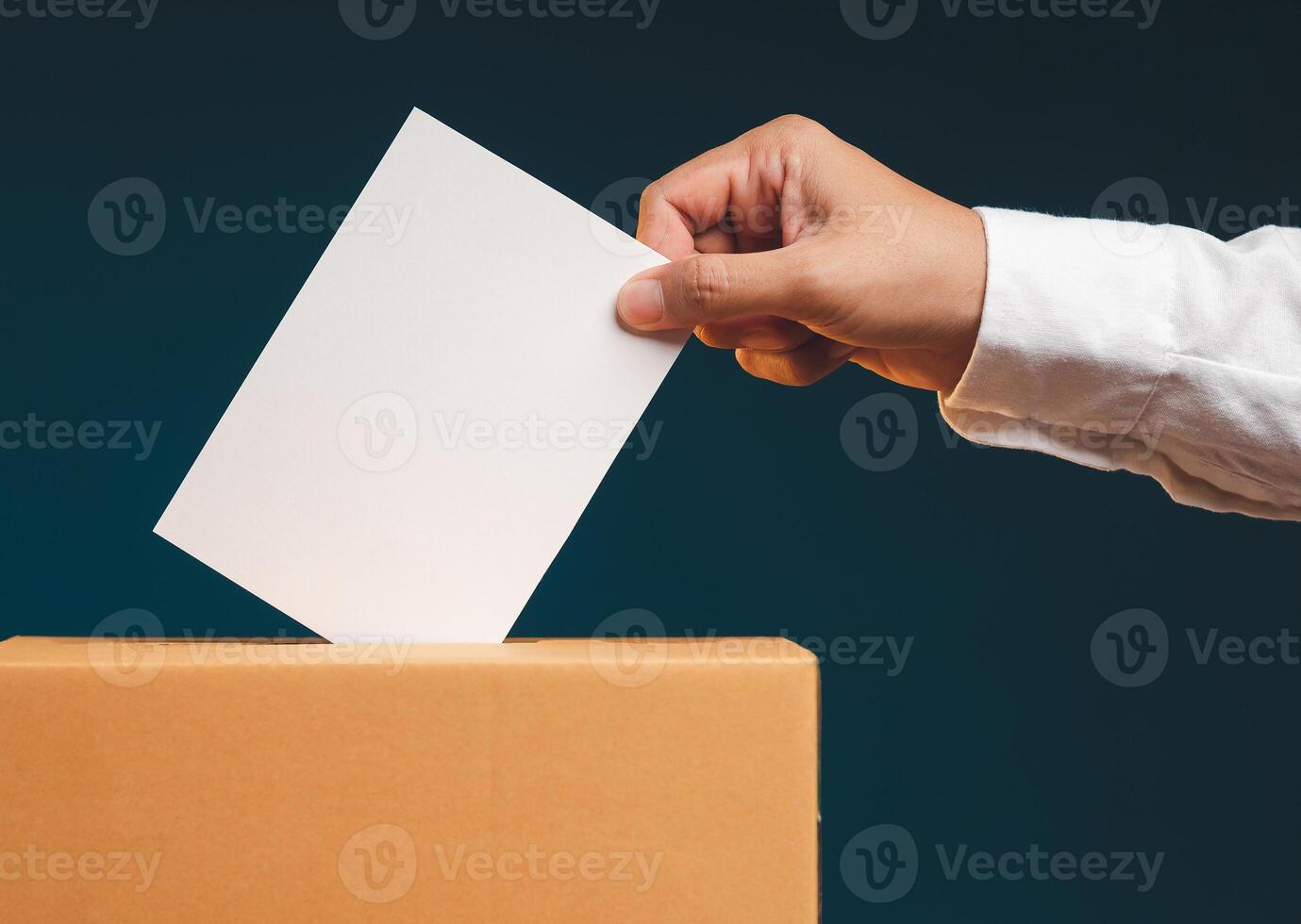 Hand voter holding ballot paper putting into the voting box at place election against a gray background. photo