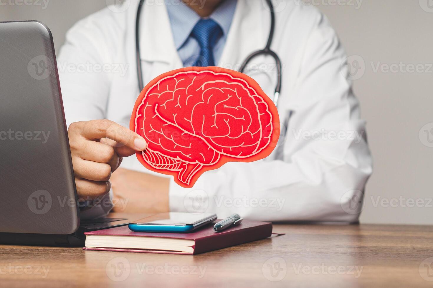 Doctor in a white coat holding a red paper brain symbol while sitting at the table photo