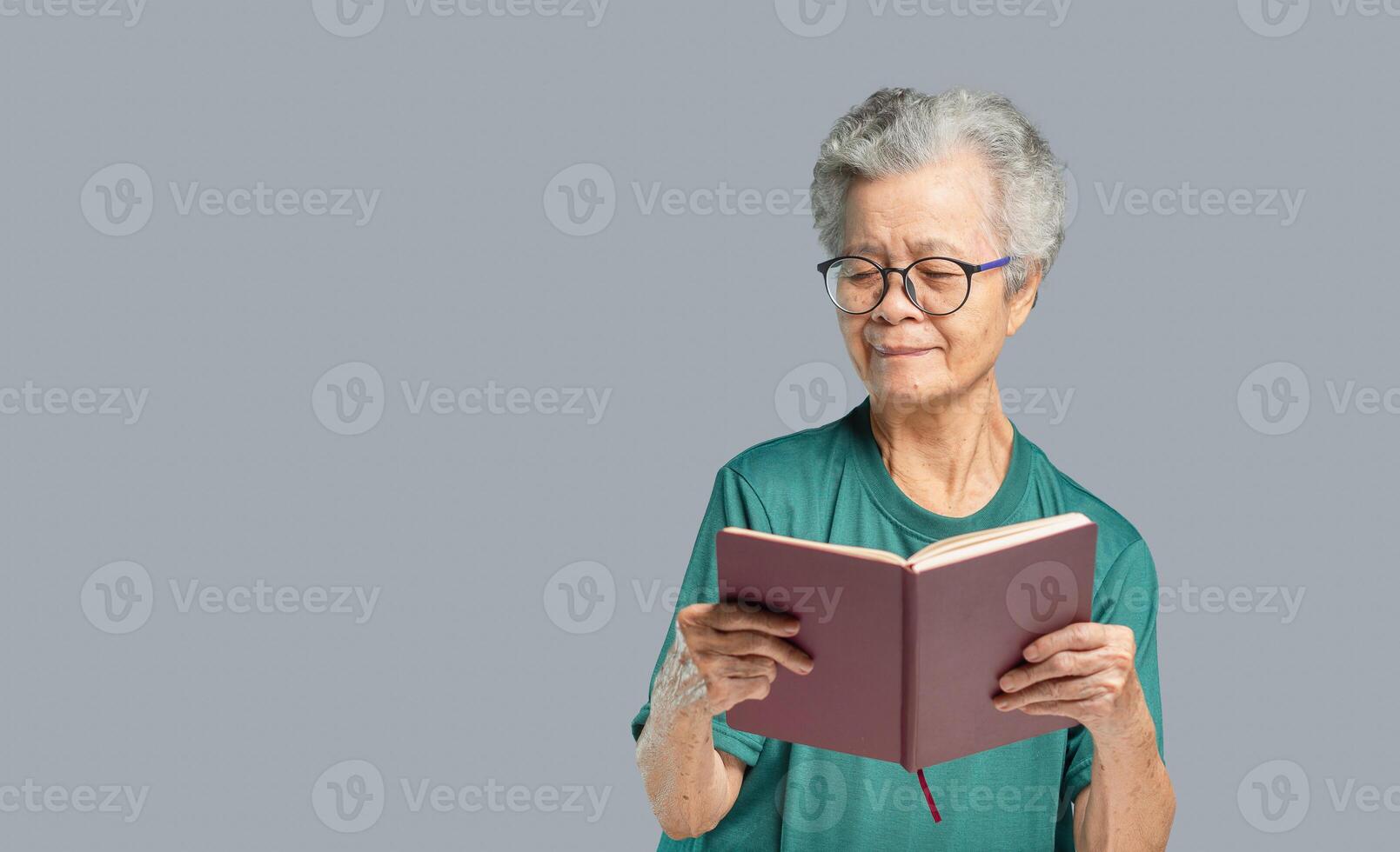 Senior woman is reading a book while standing on a gray background photo