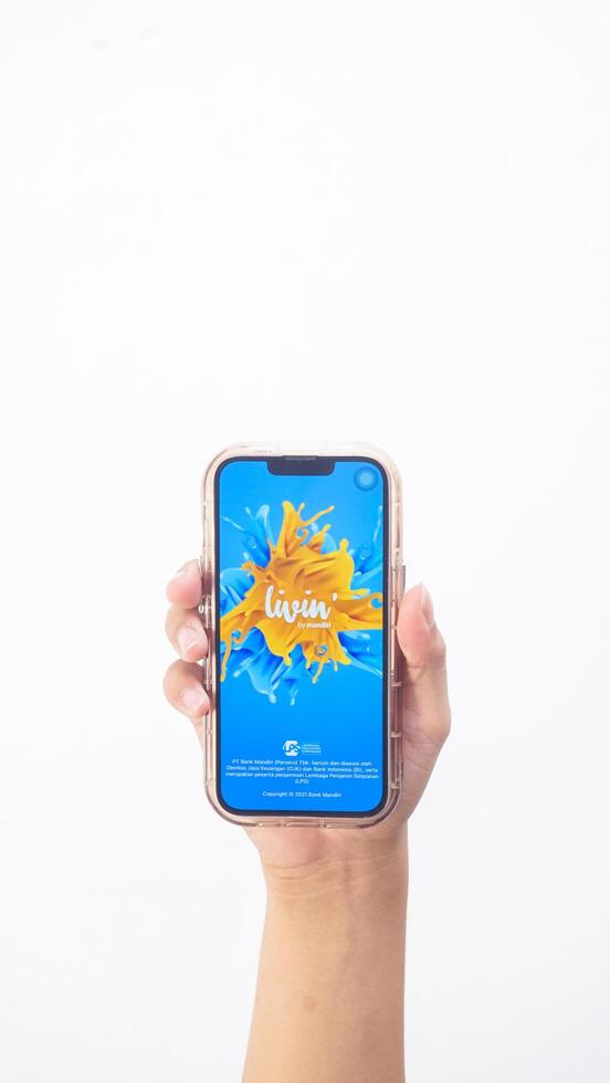 Yogyakarta, Indonesia, 2025 - Hand holding smartphone that shows Livin' by Mandiri application, a digital or mobile banking platform, on the screen isolated on white background photo