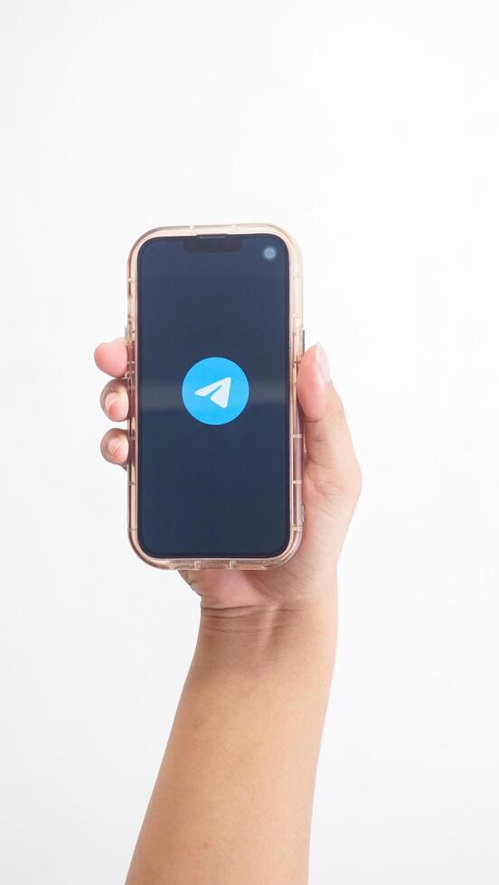 Yogyakarta, Indonesia, 2025 - Hand holding phone that shows front page of Telegram, messaging and communication platform application, on the screen isolated on white background photo