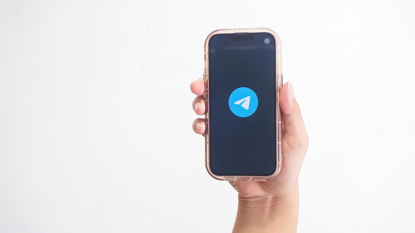 Yogyakarta, Indonesia, 2025 - Hand holding phone that shows Telegram icon, messaging and communication platform application, on the screen isolated on white background photo