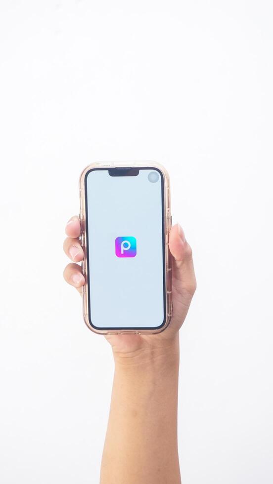 Yogyakarta, Indonesia, 2025 - Hand holding smartphone that shows Picsart application logo, a creative editing platform, on the screen isolated on white background photo