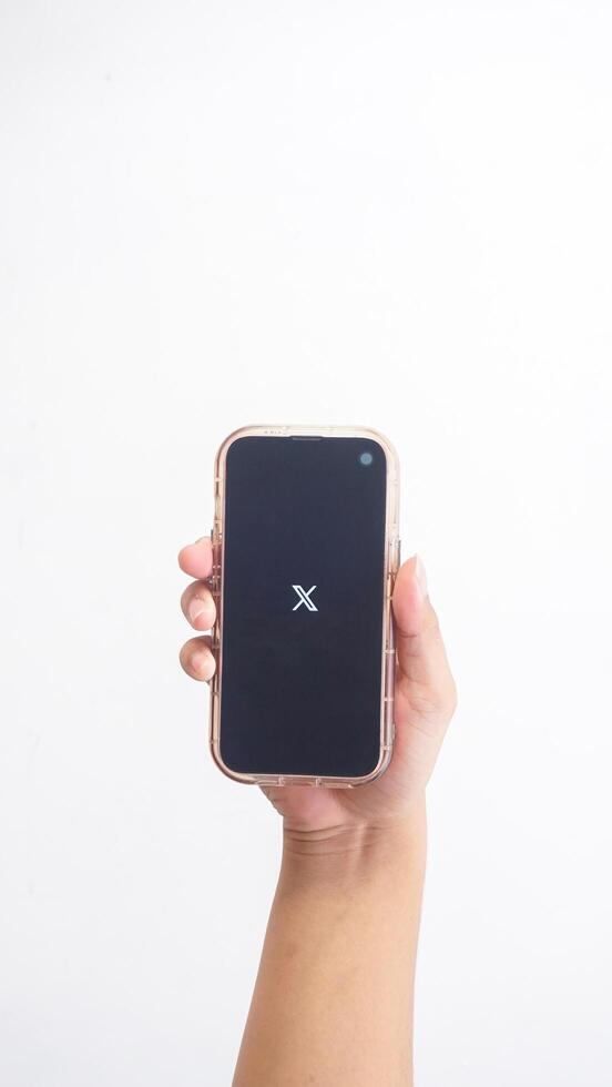 Yogyakarta, Indonesia, 2025 - Hand holding smartphone that shows front page of X application former Twitter, social media platform, on the screen isolated on white background photo