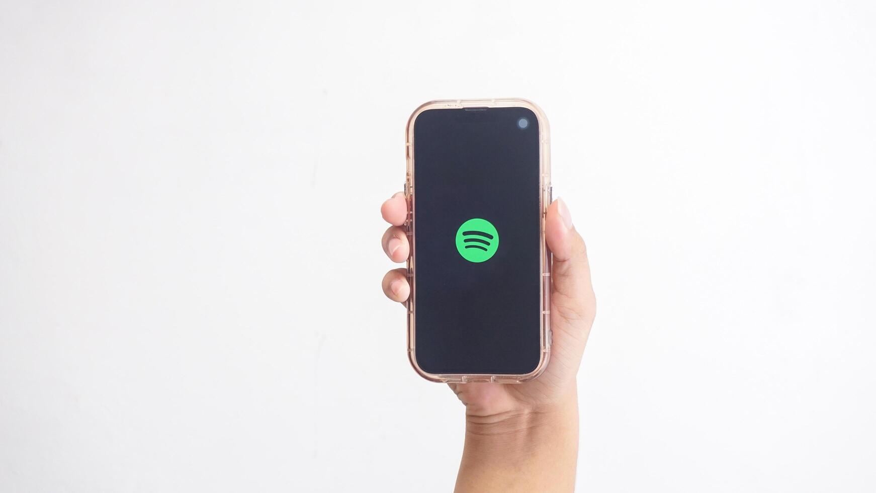 Yogyakarta, Indonesia, 2025 - Hand holding smartphone that shows Spotify icon, digital audio streaming platform application, on the screen isolated on white background photo