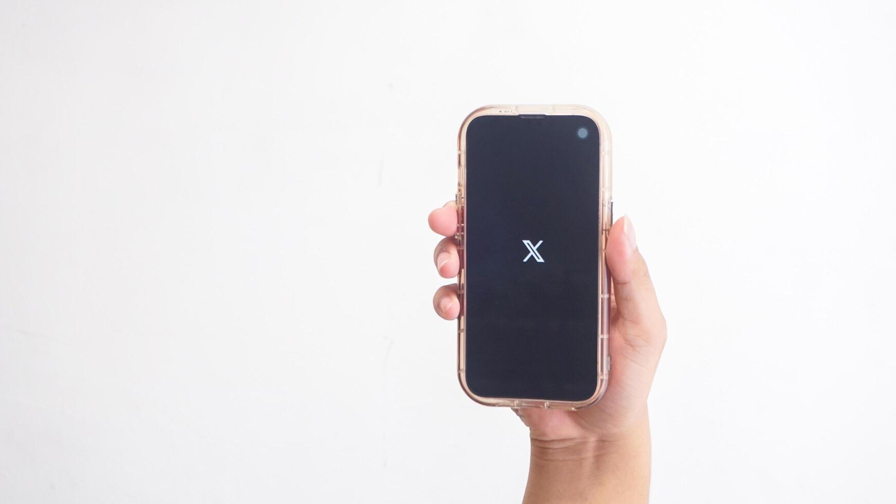 Yogyakarta, Indonesia, 2025 - Hand holding smartphone that shows X application former Twitter icon, a social media platform, on the screen isolated on white background photo