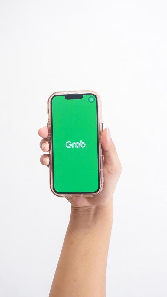 Yogyakarta, Indonesia, 2025 - Hand holdingHand holding smartphone that shows front page of Grab application, on-demand service platform, on screen isolated on white background photo