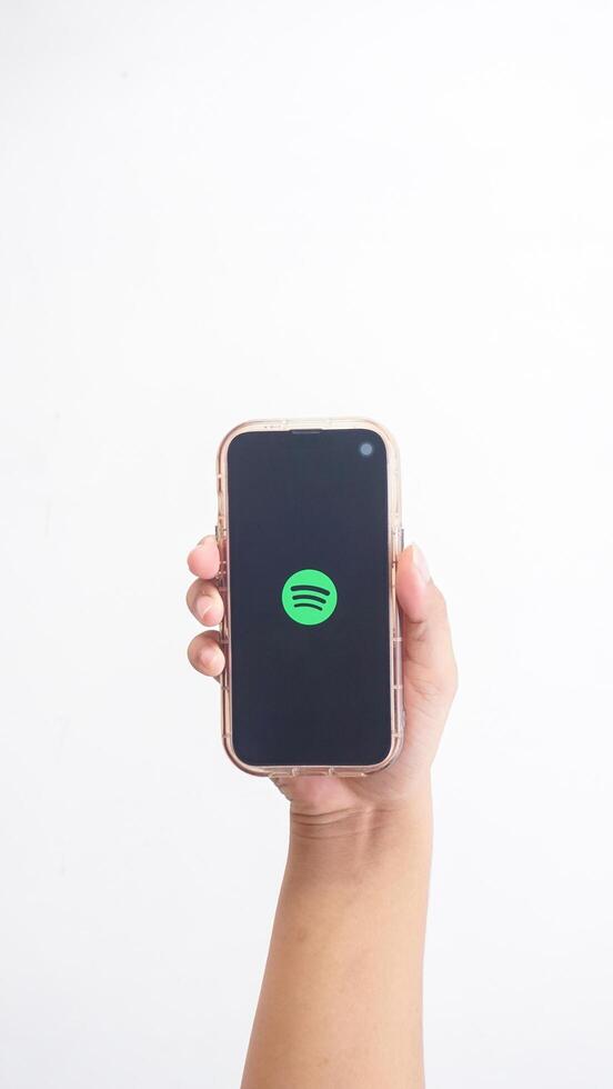 Yogyakarta, Indonesia, 2025 - Hand holding smartphone that shows front page of Spotify, digital audio streaming platform application, on the screen isolated on white background photo