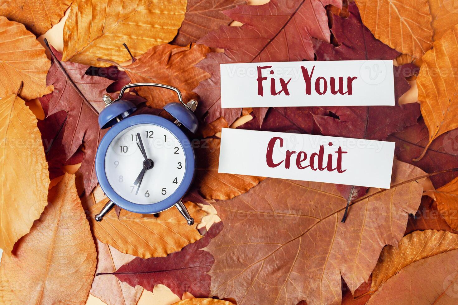 Clock surrounded by autumn leaves with Fix Your Credit written on paper symbolizing financial change and urgency photo