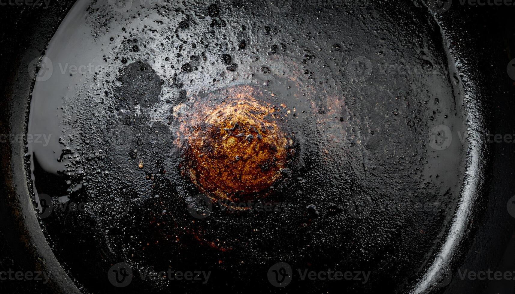 top view of burned and oily cast iron skillet with charred food residue and dark cooking grease texture for rustic kitchen or food background photo