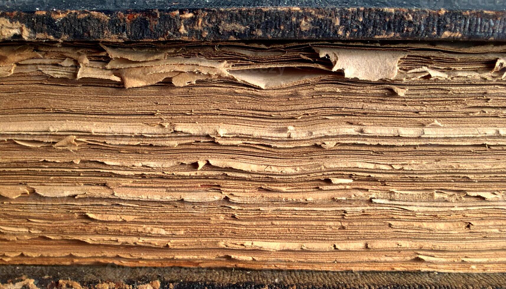 close-up side view of aged vintage book pages with frayed and wrinkled texture, old antique paper stack background, historical decay concept photo