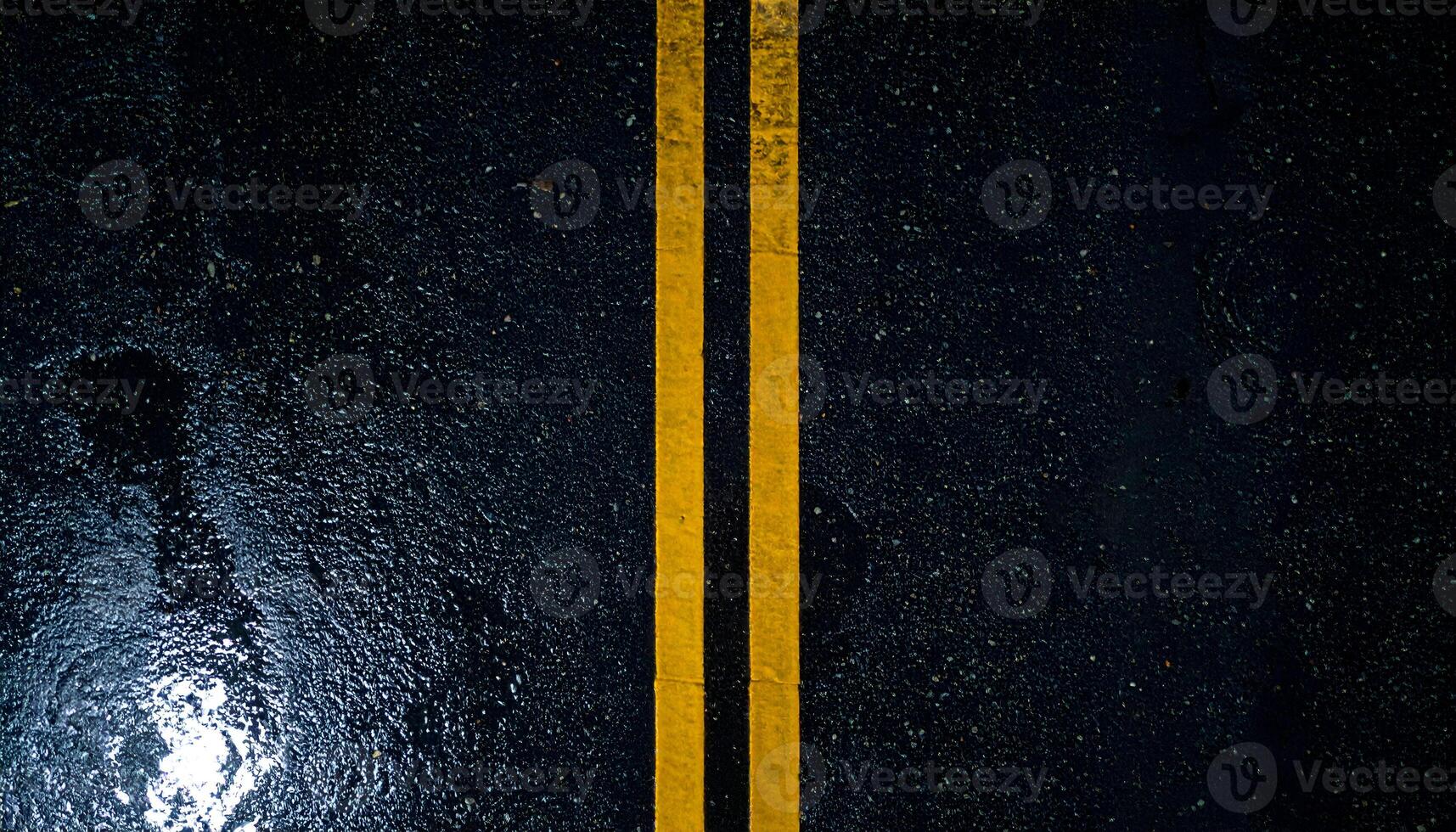 wet asphalt road at night with double yellow lines, top view of dark moody street texture with rain reflections and urban atmosphere photo