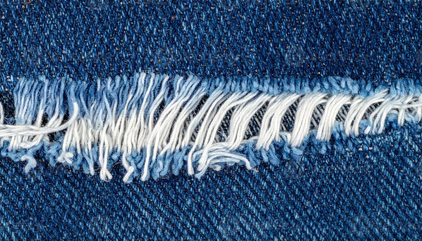 close-up frayed denim fabric with torn white threads, top view macro of distressed blue jeans texture for fashion or textile background photo