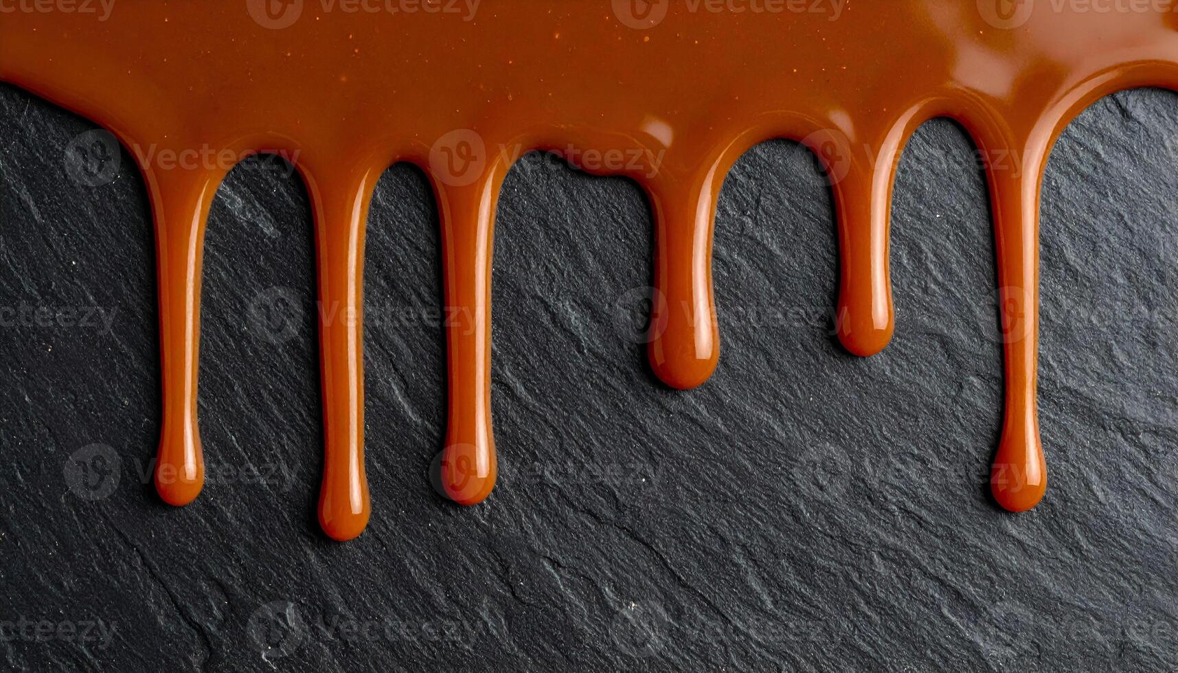 dripping caramel sauce on dark slate stone background, top view of glossy golden brown syrup flowing in abstract pattern for dessert or bakery design photo