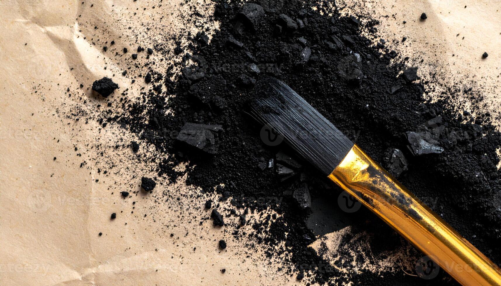 charcoal dust and crushed pieces with gold brush on brown paper texture, top view of artistic and organic material for creative, skincare or craft design photo