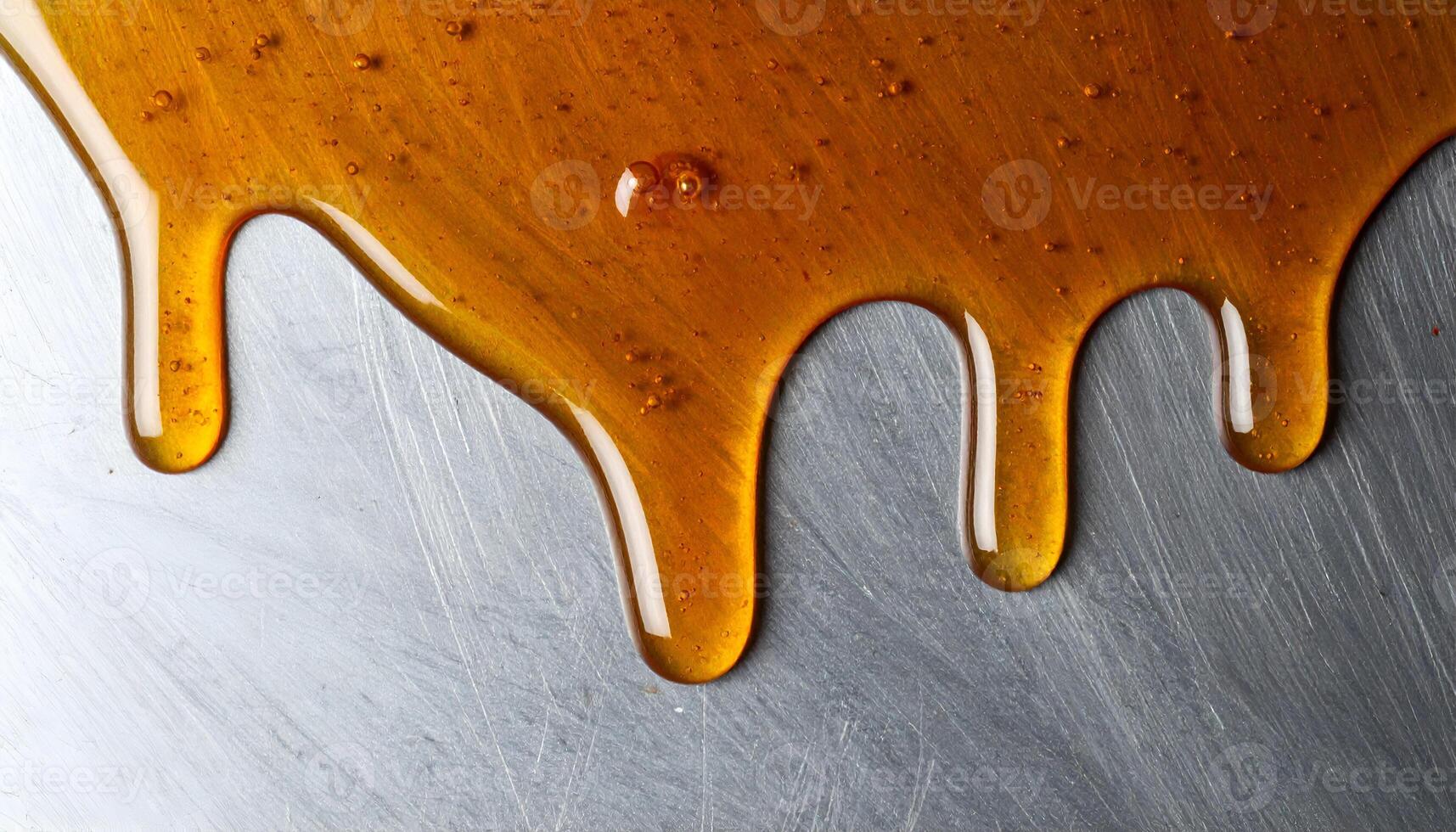 dripping honey on metal surface close-up, golden syrup flowing with glossy texture and warm highlights, macro food design background for sweet dessert or healthy ingredient concept photo