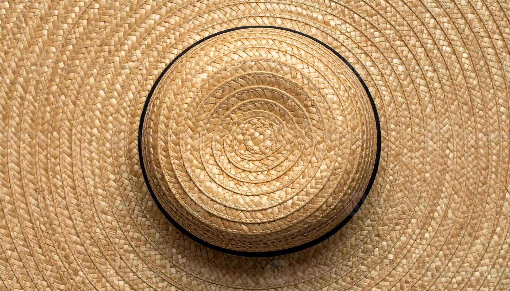 top-down view of woven straw hat with circular braided pattern, natural fiber summer accessory on textured straw background photo