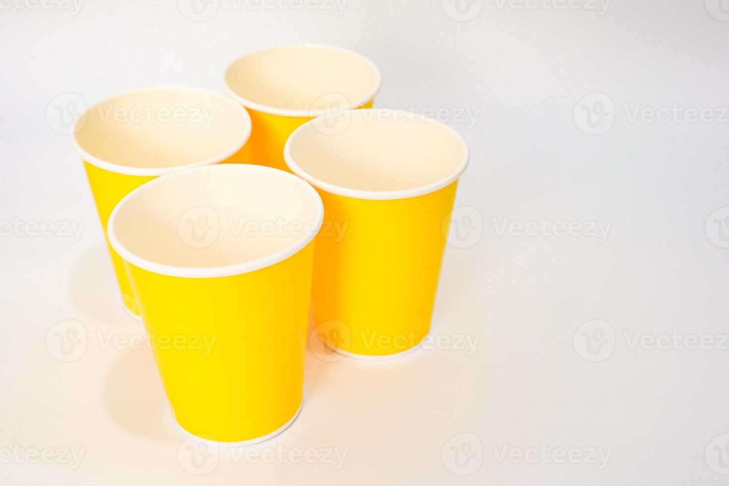 Four yellow paper cups, arranged on a white surface with soft shadows creating a minimalist composition photo