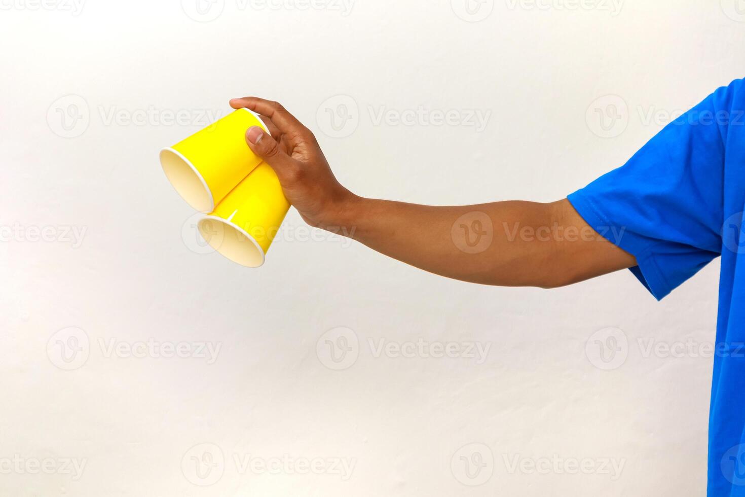 Hand holding two yellow paper cups in a blue shirt with a white background photo