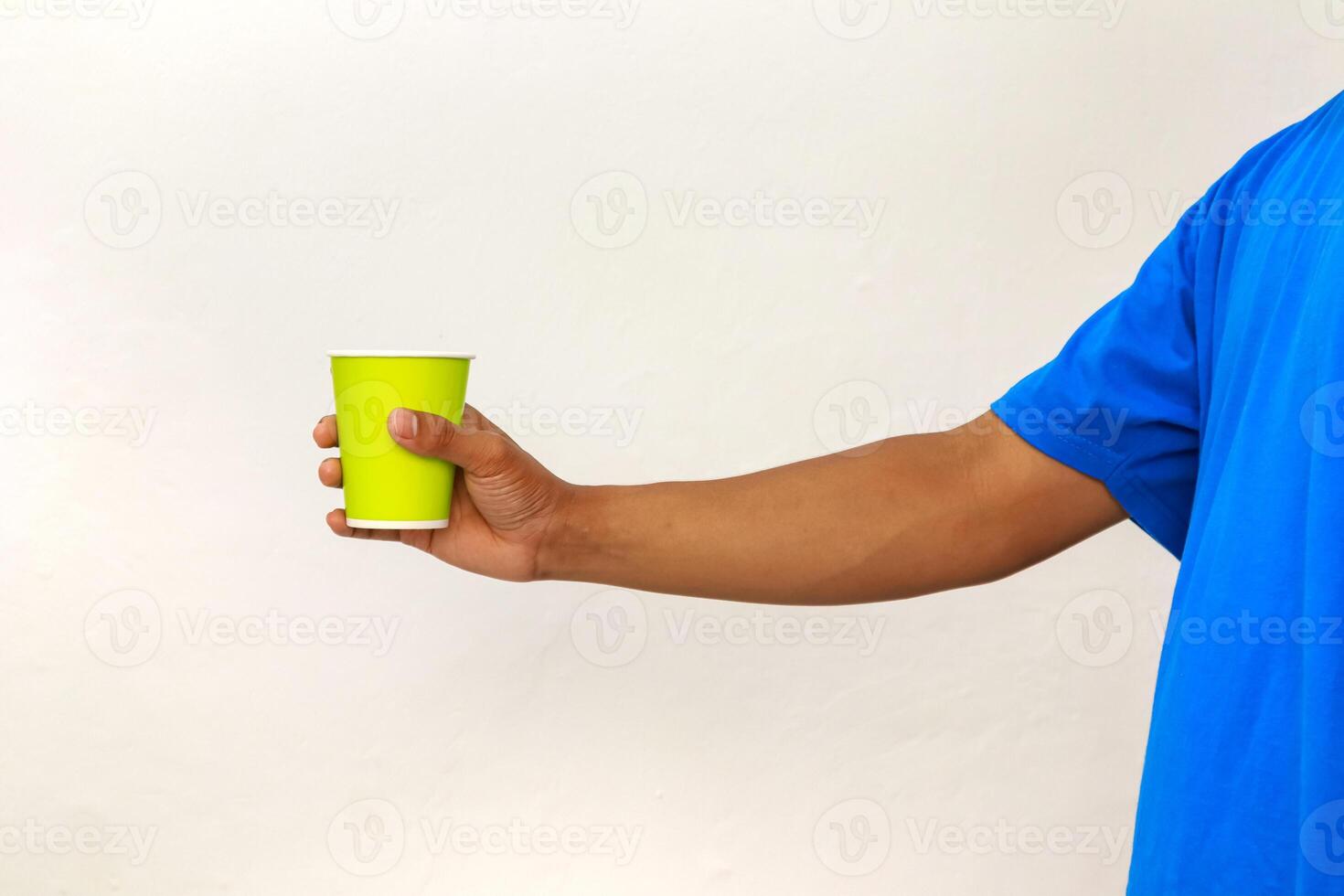 Hand in blue shirt holds a green paper cup against a white background, studio shot photo