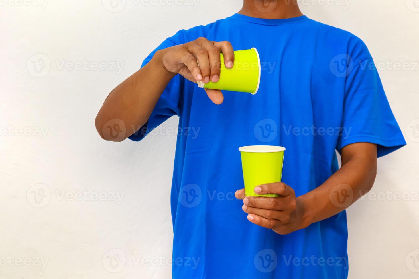 Person in Blue Shirt Pouring from a Yellow Cup into Another Against White Backdrop photo