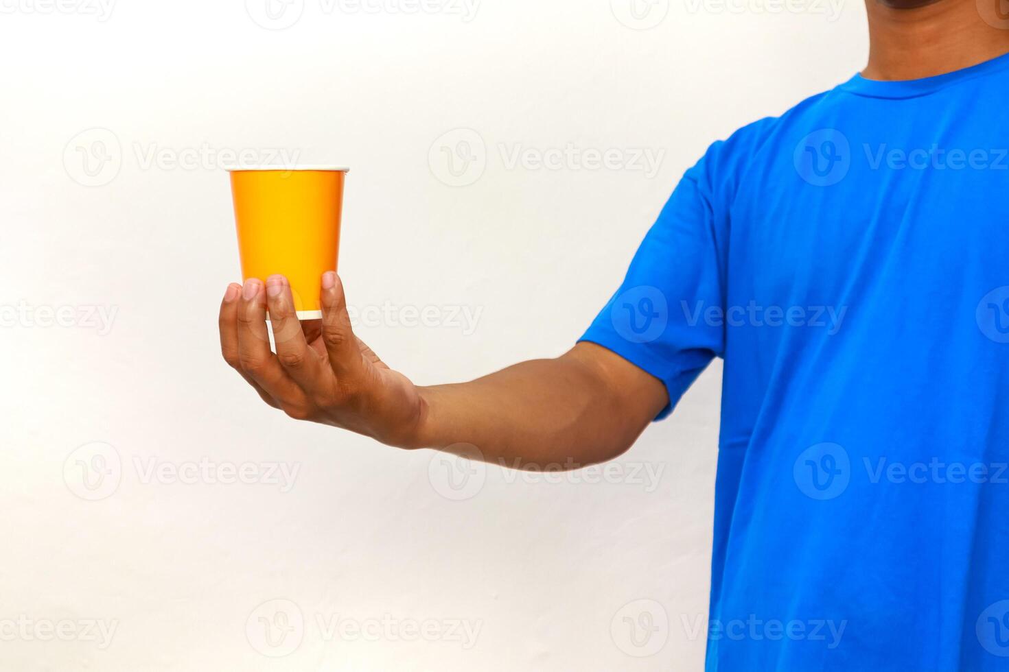 Person in Blue Shirt Holding Orange Cup Against White Background Presenting a Beverage photo