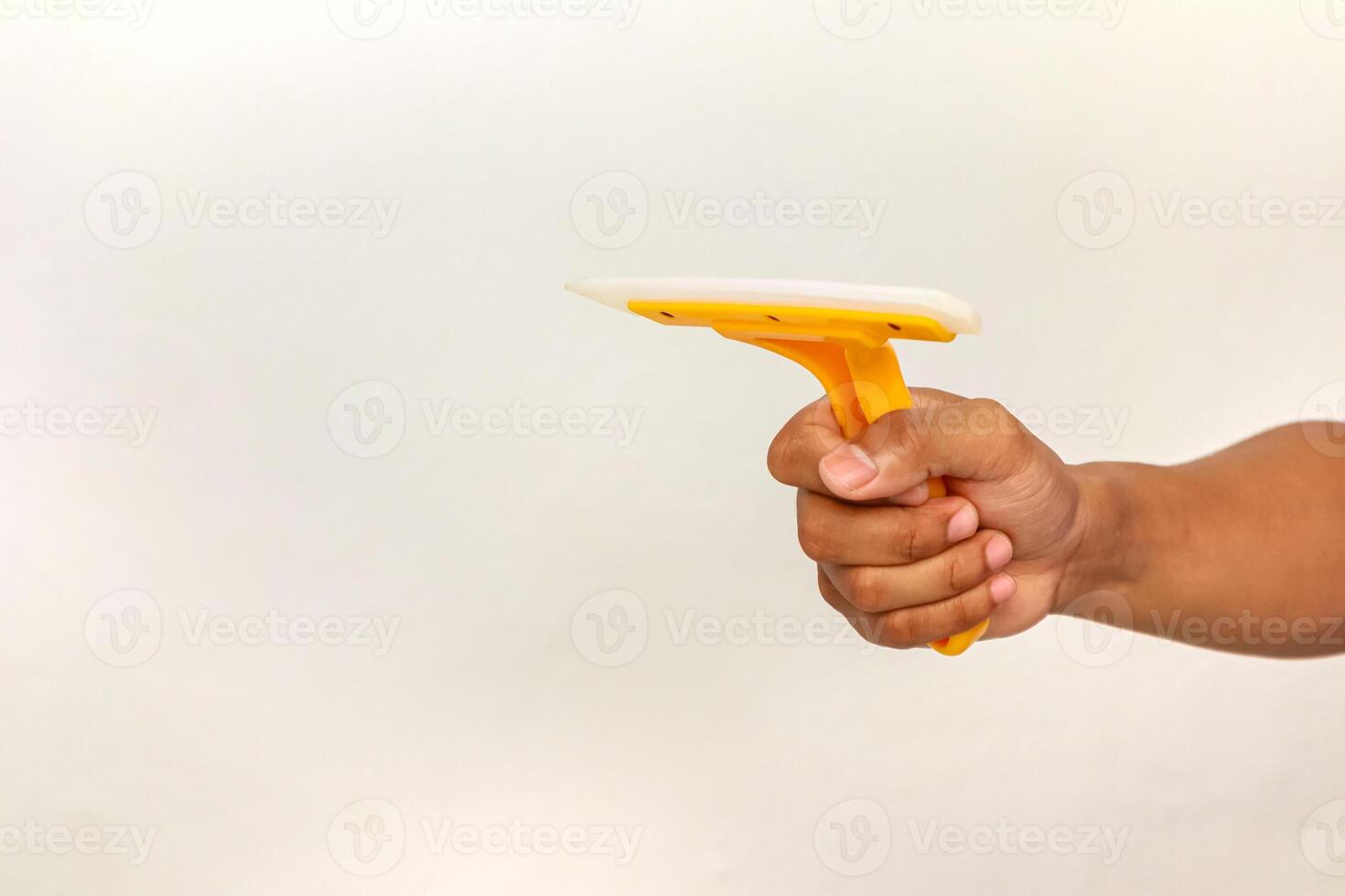 Close-up of a hand holding a yellow window squeegee against a white background ready to clean the glass photo
