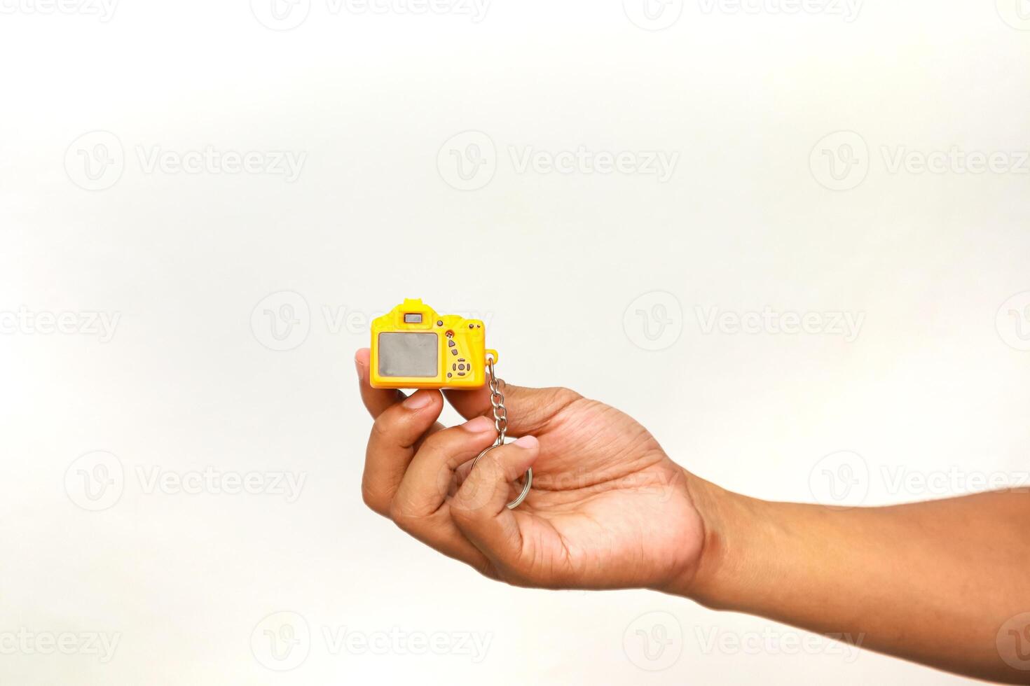 Hand Holding Miniature Yellow Camera Keychain, Close-Up on White Background photo