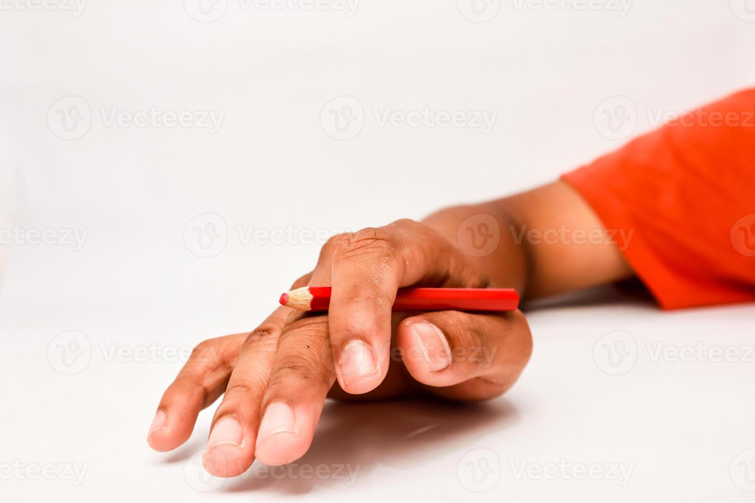 Hand holding a vibrant red pencil with an orange shirt sleeve in the background on white photo