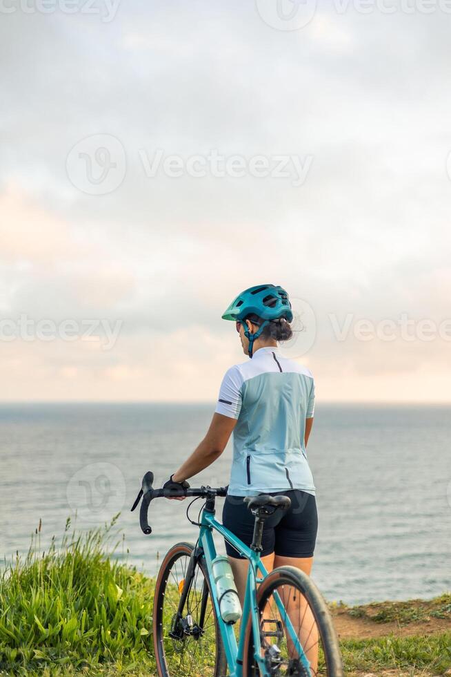 vertical woman Cyclist admiring the ocean view at sunrise from a cliff photo