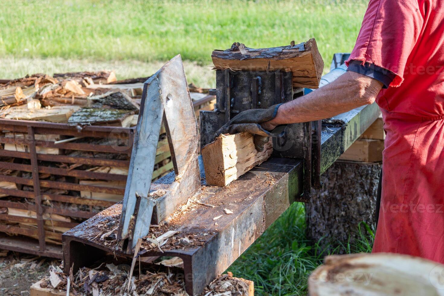 Lumberjack splitting firewood logs using hydraulic machine in countryside photo