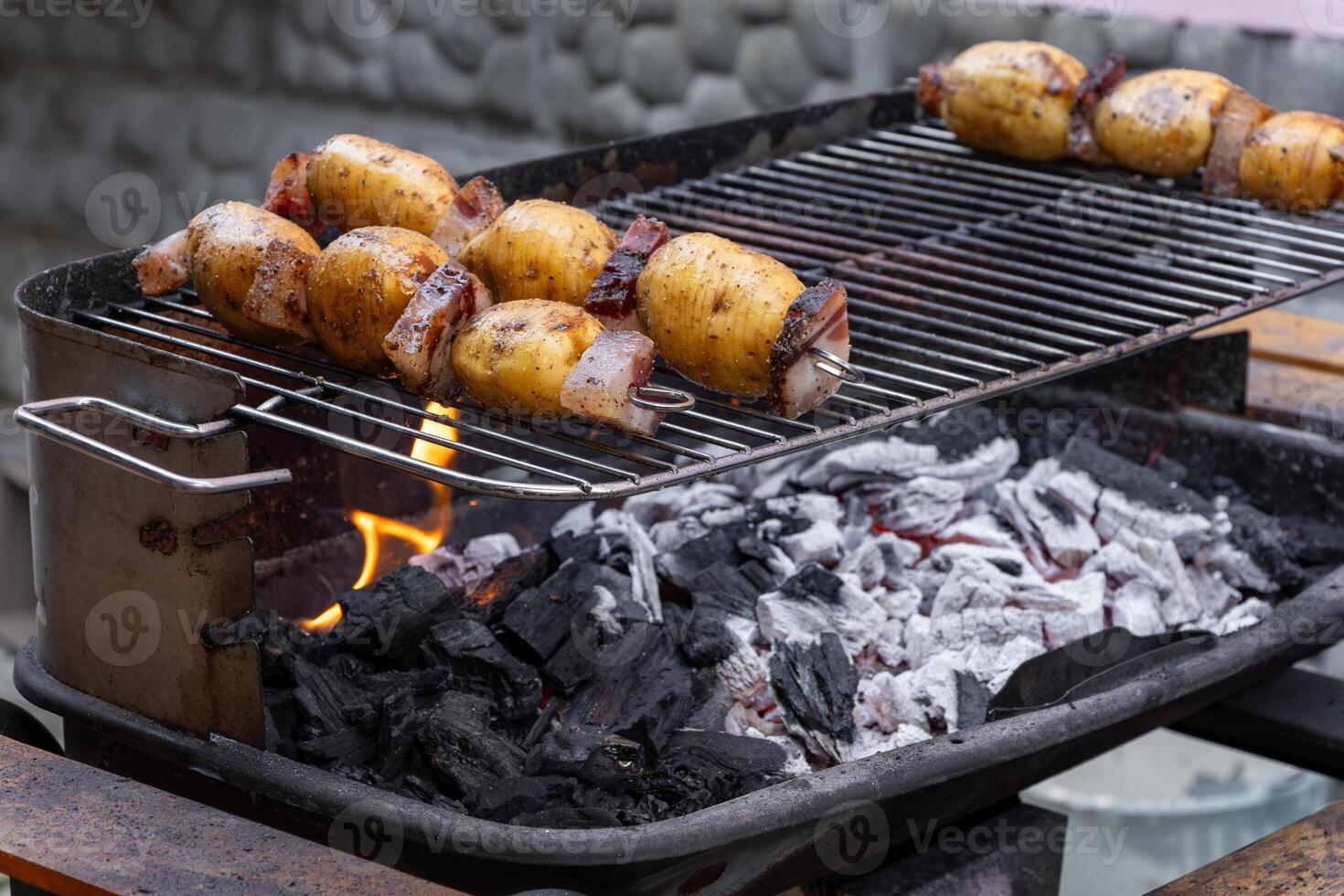 Grilling potatoes and bacon skewers on a charcoal barbecue grill photo