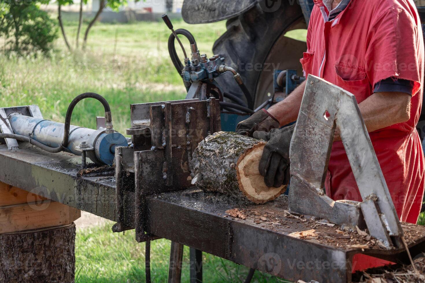 Farmer splitting firewood logs using tractor driven hydraulic log splitter machine photo