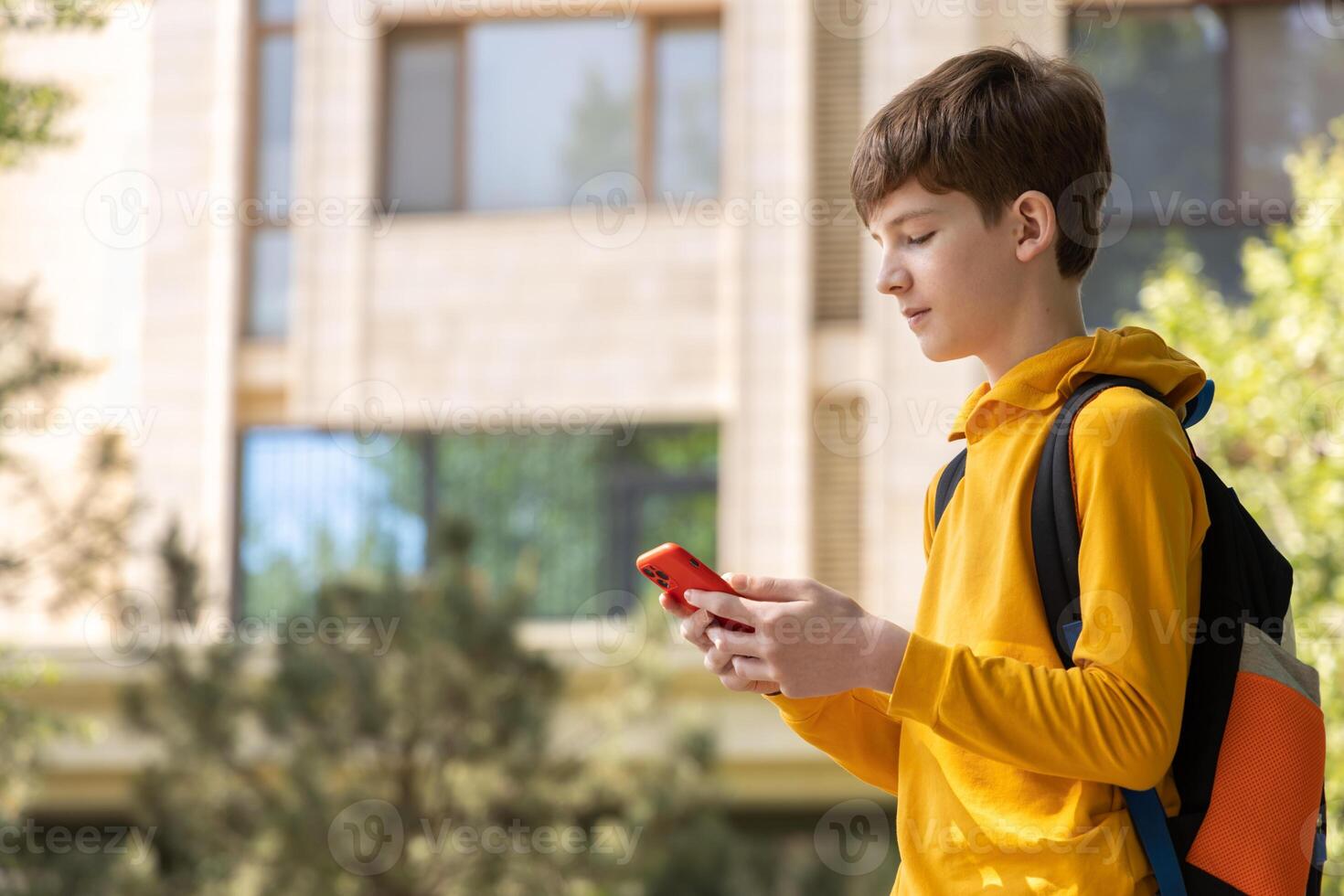 Teenage boy stands in front of an apartment building, holding a smartphone and smiling. Symbolizes digital accessibility, online communication, and modern connected lifestyle photo