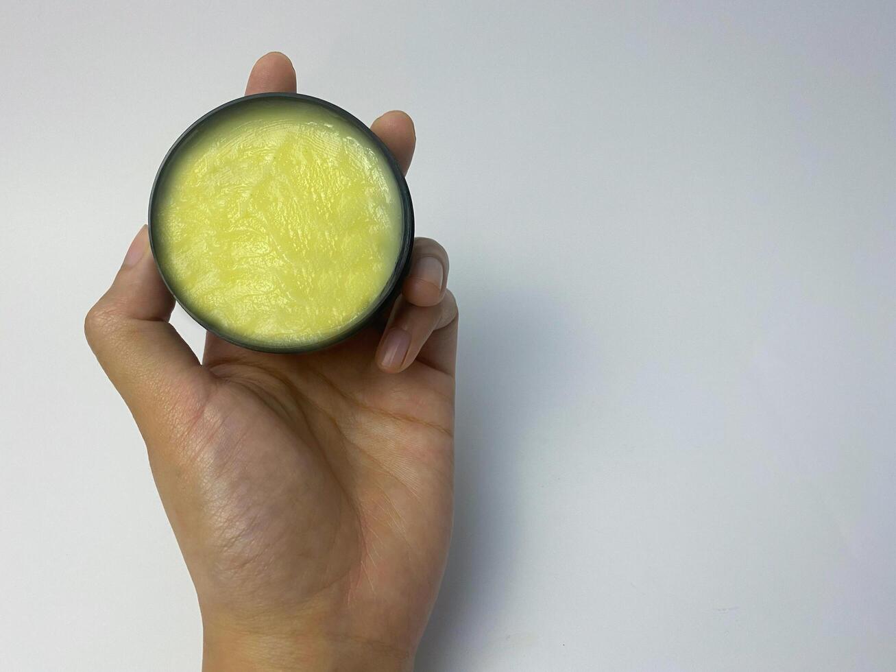Hand holding container of yellow balm for skin care or personal grooming photo
