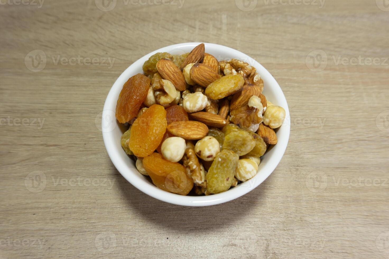 Assorted nuts and dried fruits in a white bowl on wooden surface photo