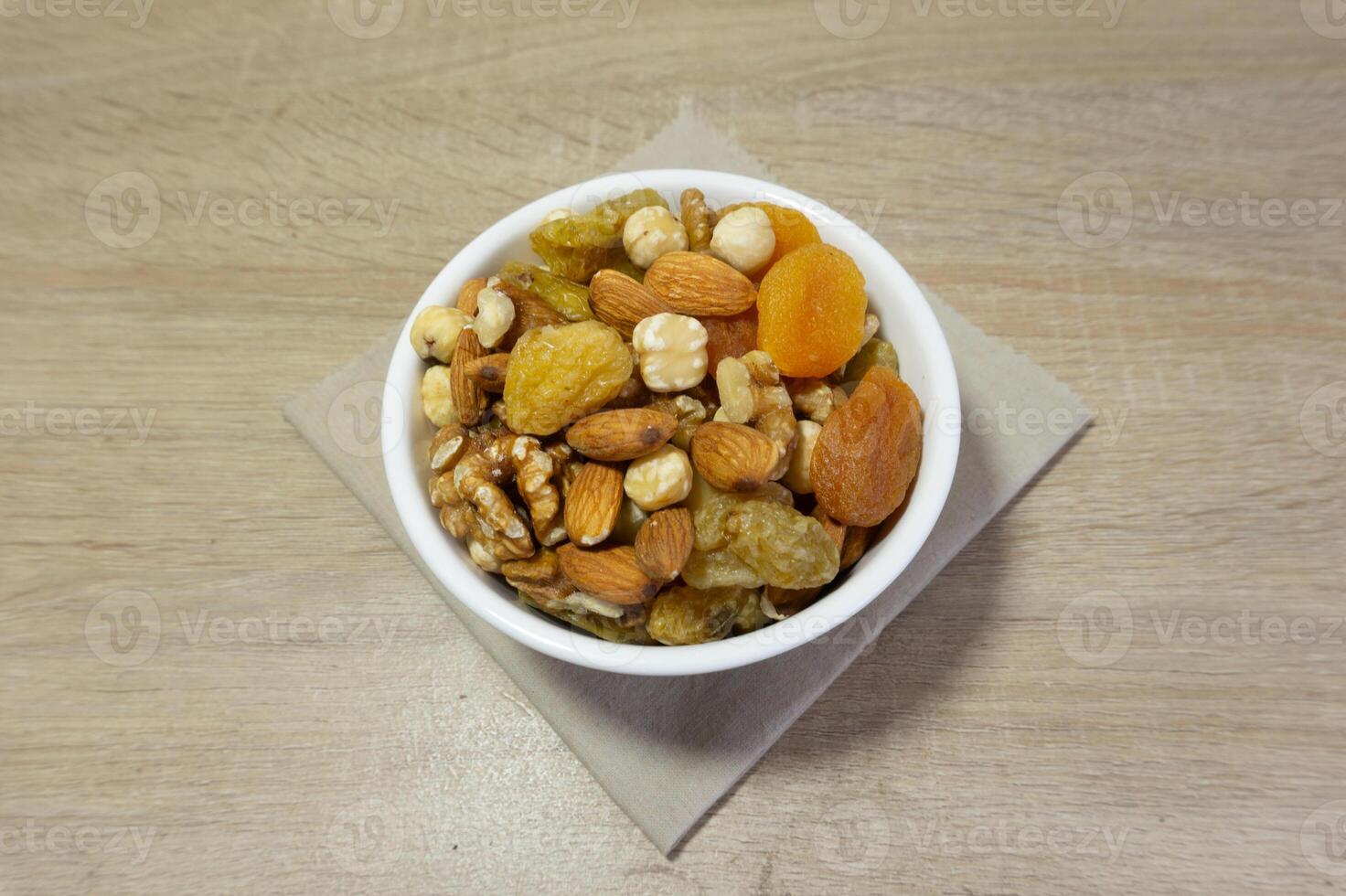 Delicious and Healthy Mix of Dried Fruits and Nuts in a White Bowl on a Wooden Surface photo