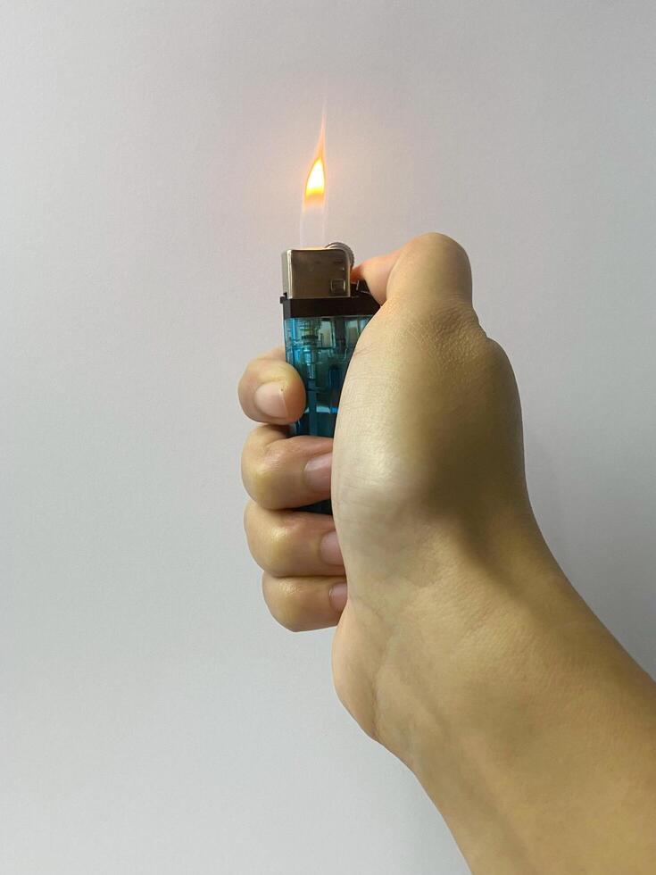 Close-up of a hand holding a lit lighter against a neutral background photo