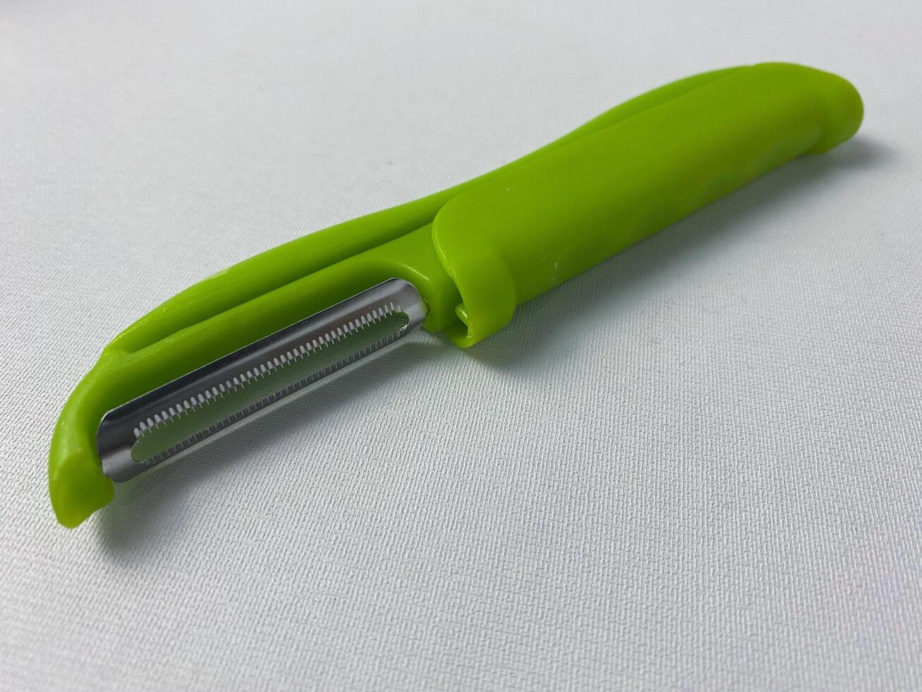 Close-up shot of a green vegetable peeler on a white surface ready for kitchen use photo