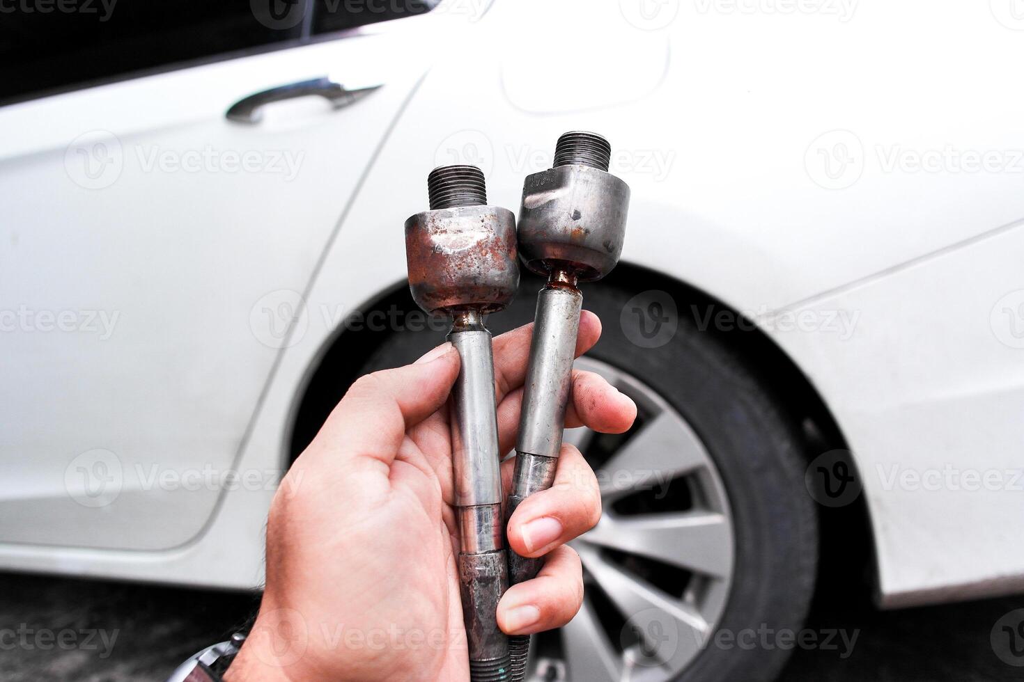 Car inner tie rods, A mechanic hand holds two automotive inner tie rods worn out, old rusty against a blurred car background. photo