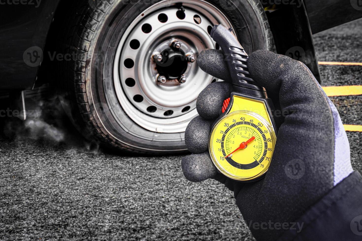 Tire Pressure Check, Auto mechanic wearing a glove checks a car tire air pressure with a yellow gauge, with the wheel and flat tire in background. photo