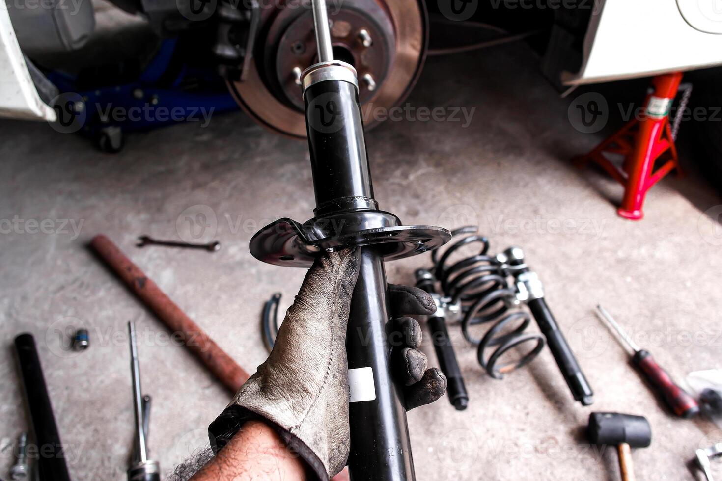 Car Shock Absorber or Strut, A mechanic hand holds a new black shock absorber or strut for replacement, surrounded by car parts and tools in a auto repair garage. photo