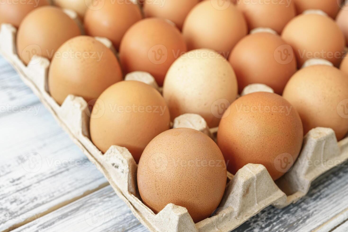 Chicken eggs in a cardboard tray on a wood background for farm and food concepts and healthy eating or cooking recipes and ingredients advertising. photo