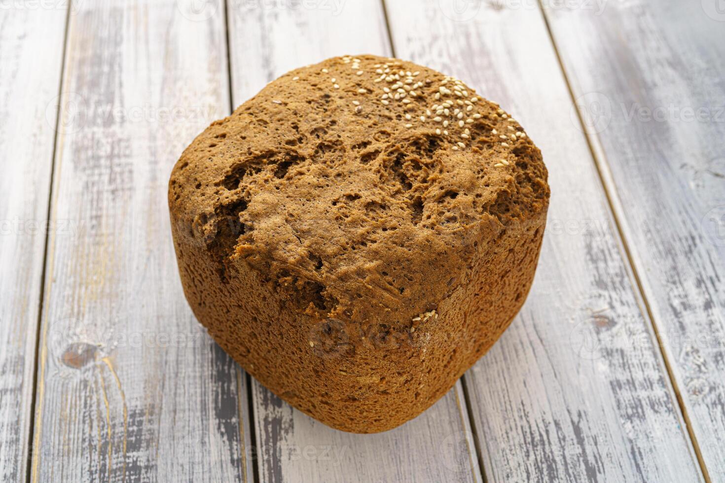 Whole grain gray bread loaf with sesame seeds and flax seeds on a rustic wooden table, healthy fresh baked snack food, homemade natural delicious bakery product concept. photo