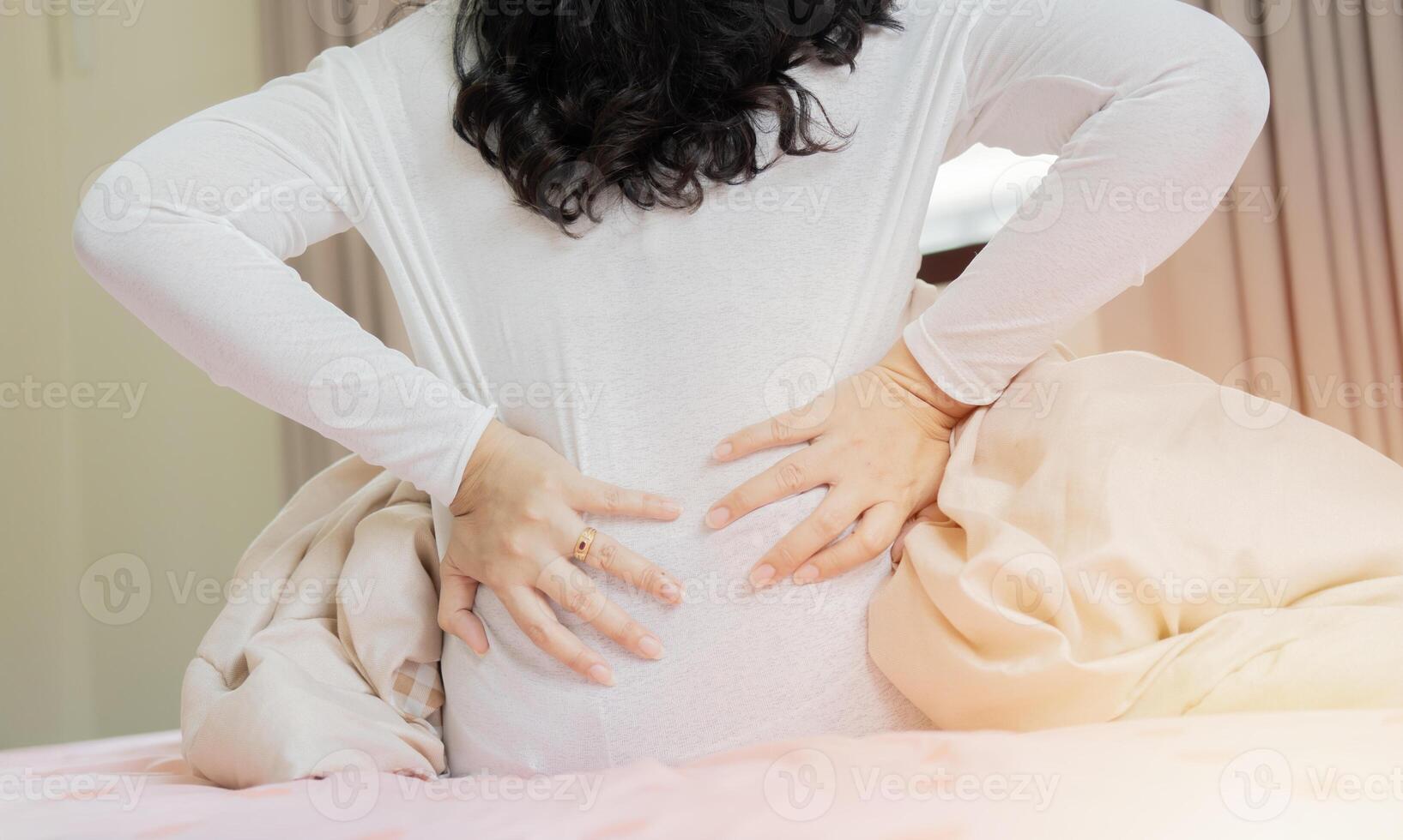 Unhealthy unhappy woman sitting on bed, massaging back, suffering from painful photo