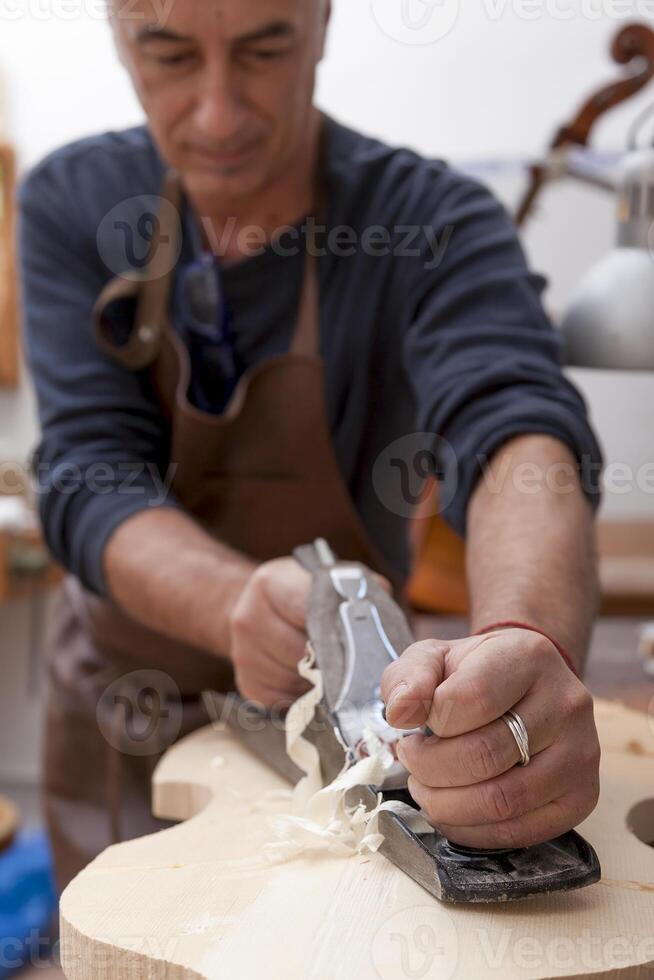 skilled violin maker in the workshop planing a piece of wood to make a violin - focus on hand photo